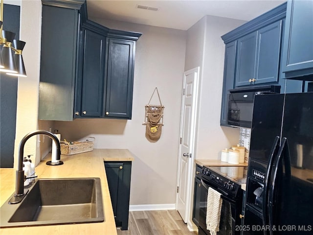kitchen with visible vents, a sink, light wood-style flooring, black appliances, and blue cabinetry