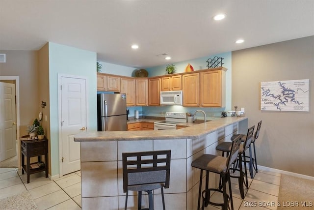 kitchen with a kitchen breakfast bar, light tile patterned floors, white appliances, and kitchen peninsula