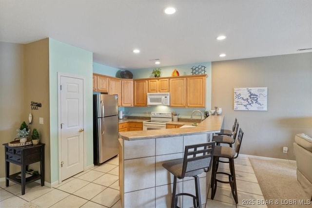 kitchen featuring sink, light tile patterned floors, a kitchen breakfast bar, kitchen peninsula, and white appliances