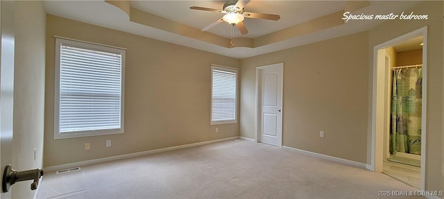 empty room featuring ceiling fan, light colored carpet, and a raised ceiling