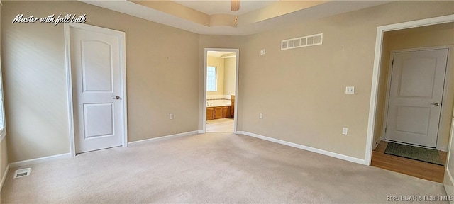 unfurnished bedroom featuring light colored carpet, ensuite bathroom, and a tray ceiling