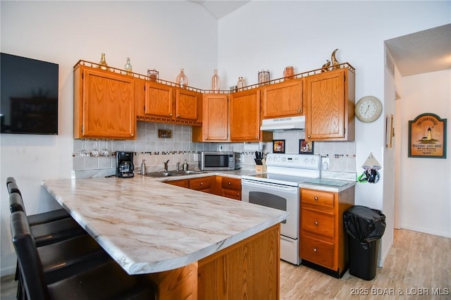 kitchen featuring sink, a breakfast bar area, white range with electric stovetop, and kitchen peninsula