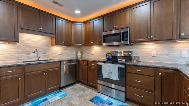 kitchen featuring dark brown cabinetry, sink, dark stone counters, stainless steel appliances, and backsplash