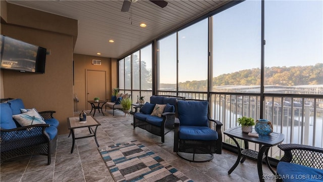 sunroom with ceiling fan and a water view