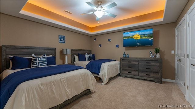 bedroom featuring ceiling fan, light colored carpet, and a tray ceiling