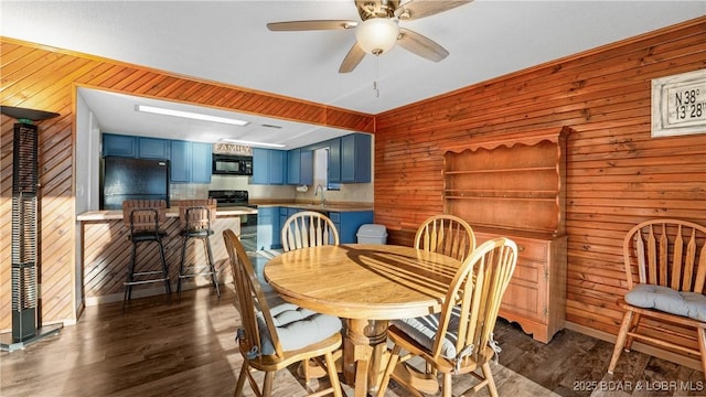 dining room featuring ceiling fan, wooden walls, sink, and dark hardwood / wood-style flooring