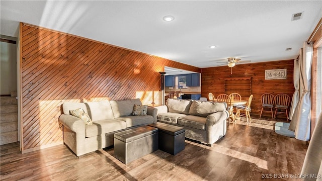 living room featuring wood-type flooring, wooden walls, and ceiling fan