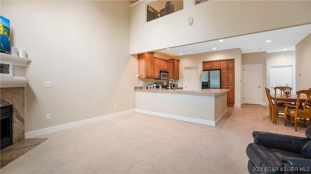 kitchen with a premium fireplace, appliances with stainless steel finishes, a towering ceiling, light carpet, and kitchen peninsula