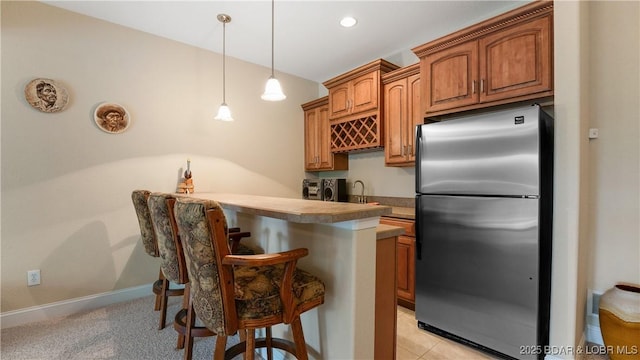 kitchen with sink, a breakfast bar area, stainless steel refrigerator, decorative light fixtures, and kitchen peninsula