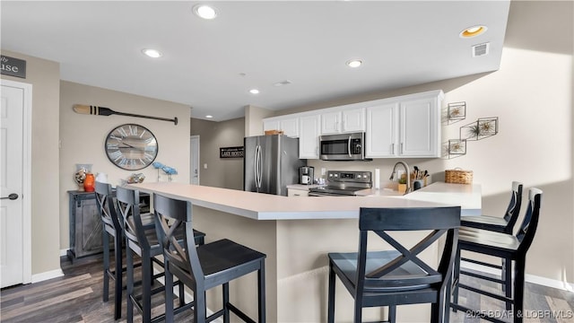 kitchen featuring dark wood-type flooring, a kitchen bar, white cabinetry, appliances with stainless steel finishes, and kitchen peninsula