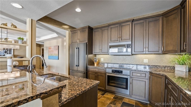 kitchen with appliances with stainless steel finishes, sink, dark stone countertops, and dark brown cabinets