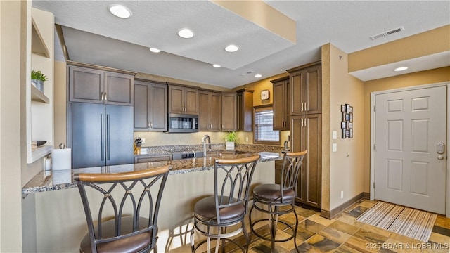 kitchen featuring a kitchen bar, a textured ceiling, dark stone counters, kitchen peninsula, and stainless steel appliances