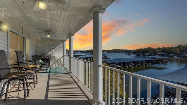 balcony at dusk featuring a water view and ceiling fan