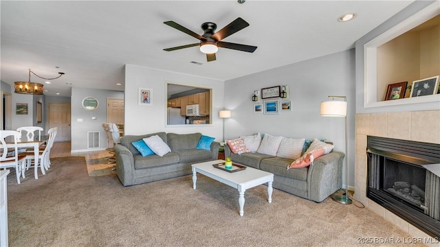 living area with visible vents, a tiled fireplace, ceiling fan with notable chandelier, recessed lighting, and carpet