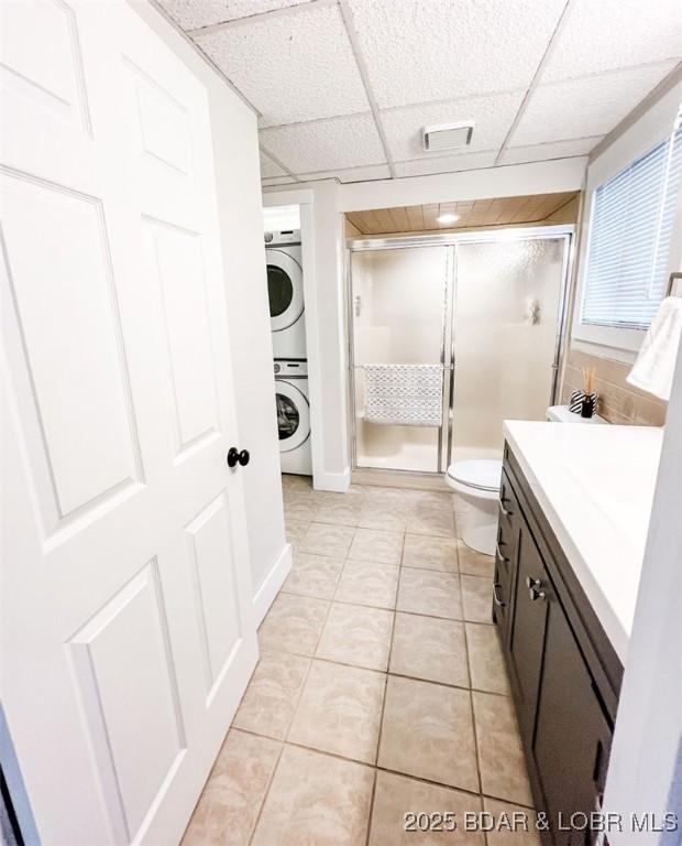 bathroom with vanity, stacked washer / drying machine, an enclosed shower, toilet, and tile patterned floors