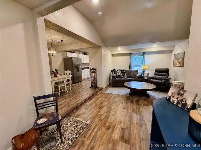 living room with a notable chandelier, hardwood / wood-style flooring, and vaulted ceiling