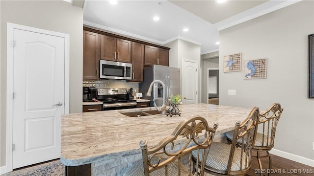 kitchen featuring crown molding, a breakfast bar area, dark brown cabinets, stainless steel appliances, and light stone countertops