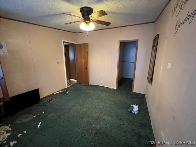 interior space featuring dark colored carpet, ornamental molding, ceiling fan, and a textured ceiling