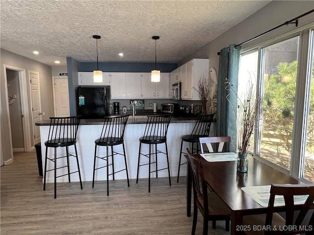 kitchen with white cabinetry, hanging light fixtures, light hardwood / wood-style floors, black fridge, and a textured ceiling