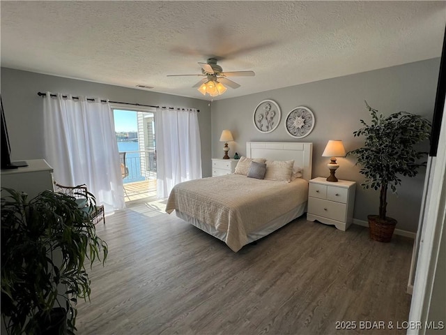 bedroom featuring a water view, a textured ceiling, access to outside, hardwood / wood-style flooring, and ceiling fan