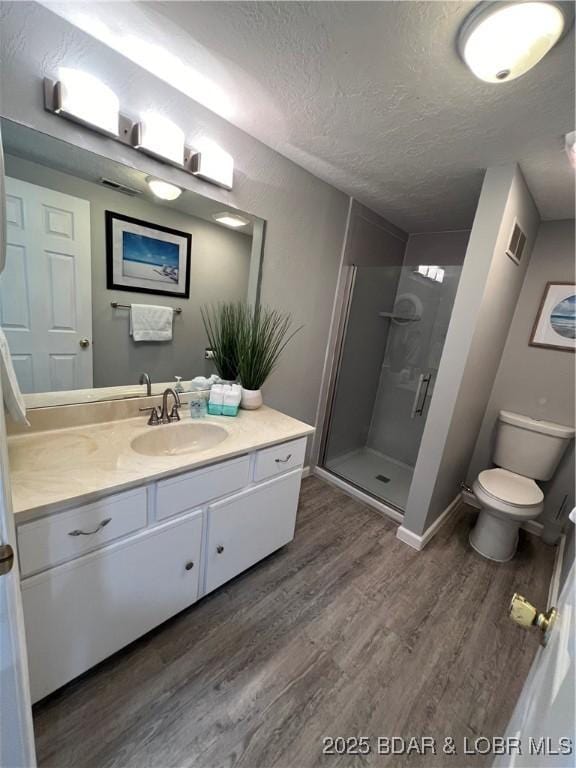 bathroom featuring hardwood / wood-style floors, vanity, walk in shower, toilet, and a textured ceiling