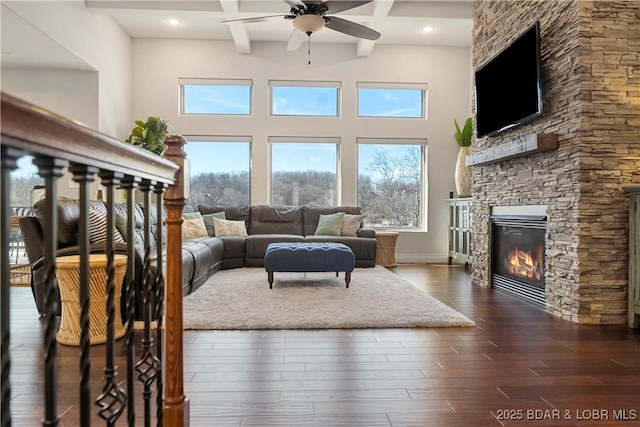 living room featuring a stone fireplace, dark hardwood / wood-style flooring, coffered ceiling, ceiling fan, and beam ceiling