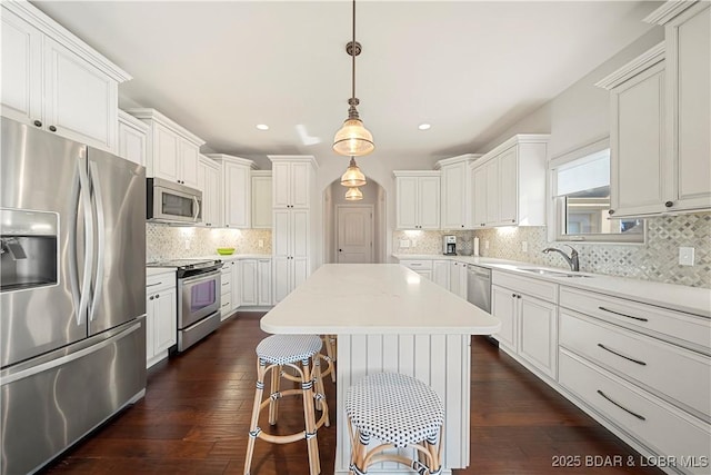 kitchen with sink, white cabinetry, stainless steel appliances, a kitchen island, and decorative light fixtures