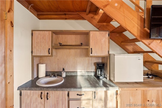 kitchen featuring sink, light brown cabinets, wooden ceiling, and refrigerator