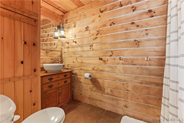 bathroom with sink, tile patterned floors, wooden walls, and toilet