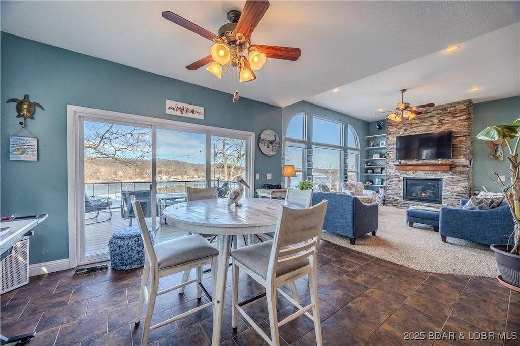 dining room with a stone fireplace, built in features, and ceiling fan