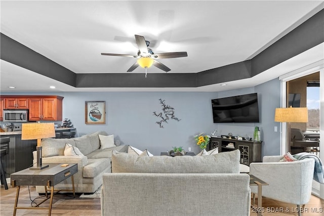 living room featuring light wood-type flooring, ceiling fan, and a tray ceiling