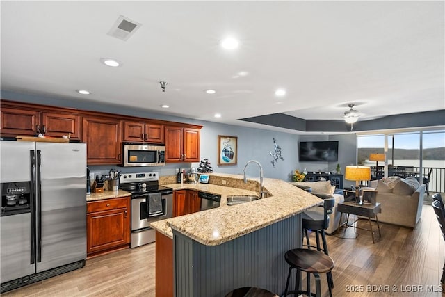 kitchen featuring sink, appliances with stainless steel finishes, light stone counters, light hardwood / wood-style floors, and a kitchen bar