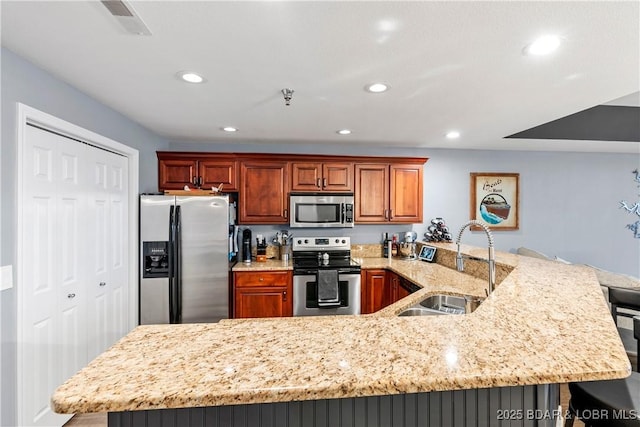 kitchen featuring sink, a breakfast bar, appliances with stainless steel finishes, light stone counters, and kitchen peninsula