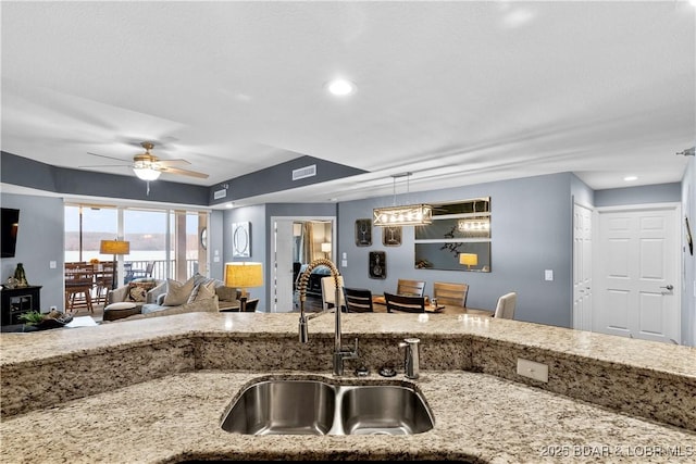 kitchen featuring hanging light fixtures, light stone countertops, sink, and ceiling fan