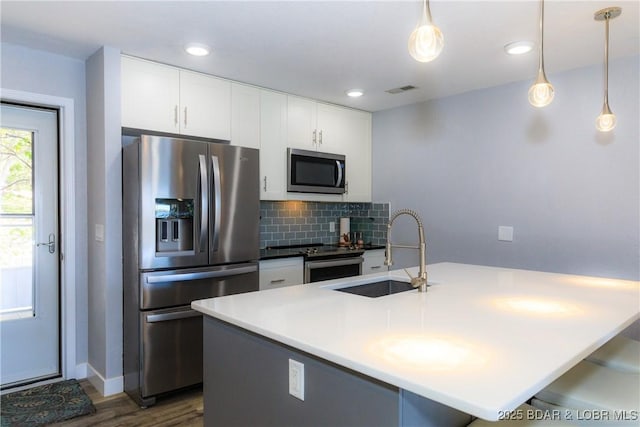 kitchen with stainless steel appliances, sink, a kitchen island with sink, and decorative light fixtures