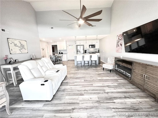 living room with high vaulted ceiling, light hardwood / wood-style floors, and ceiling fan