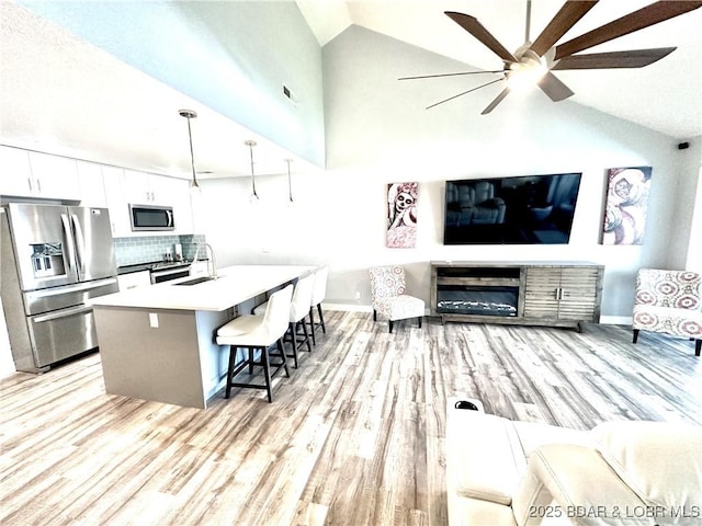 living room with ceiling fan, high vaulted ceiling, sink, and light hardwood / wood-style floors