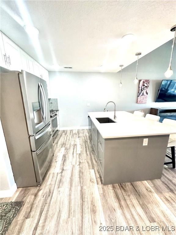 kitchen featuring appliances with stainless steel finishes, pendant lighting, sink, white cabinets, and a kitchen bar