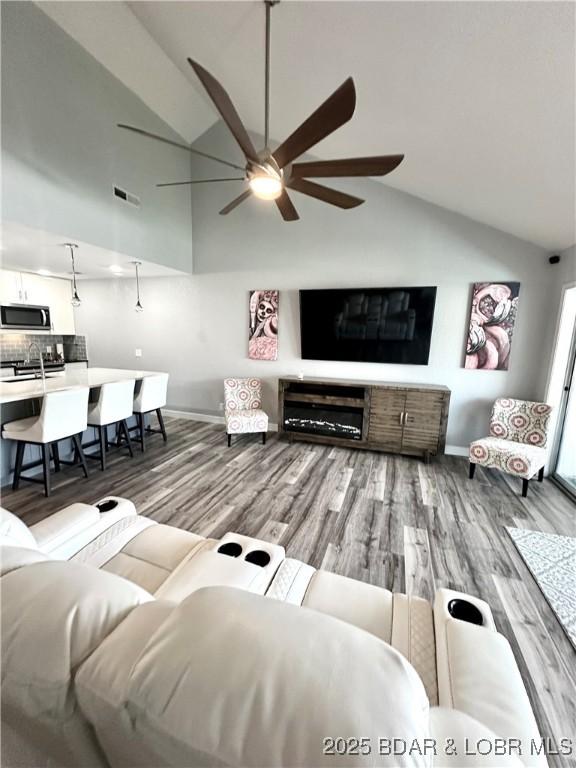 living room with wood-type flooring, ceiling fan, and high vaulted ceiling