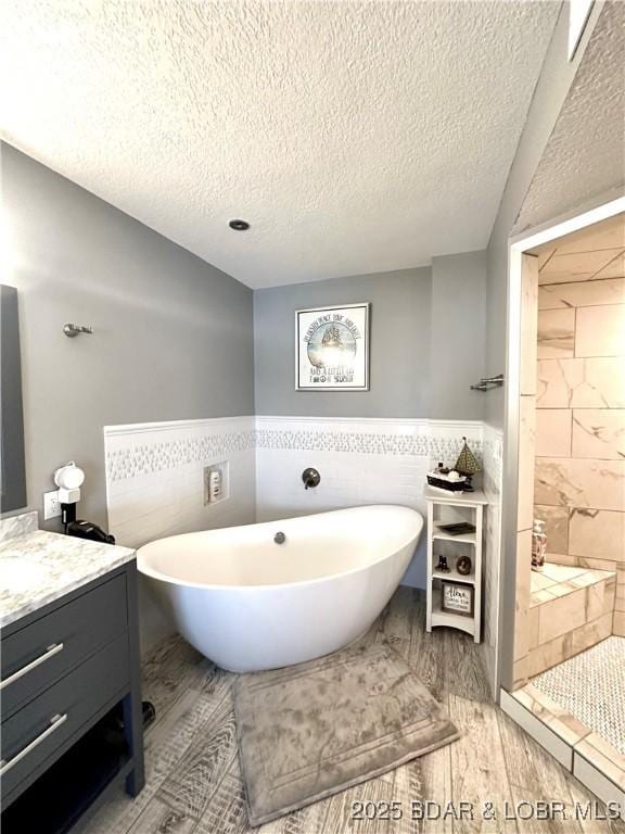 bathroom featuring tile walls, vanity, wood-type flooring, a textured ceiling, and shower with separate bathtub