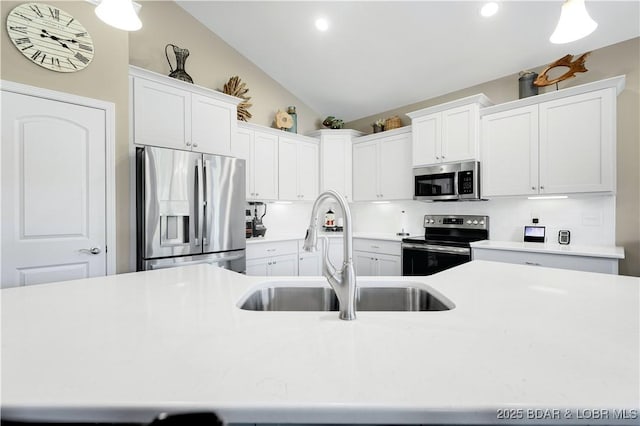 kitchen with vaulted ceiling, appliances with stainless steel finishes, white cabinetry, sink, and a center island with sink