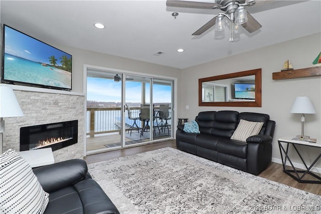 living room with ceiling fan, wood-type flooring, and a stone fireplace