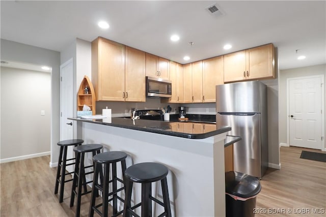 kitchen featuring appliances with stainless steel finishes, light brown cabinets, a kitchen bar, and light hardwood / wood-style flooring