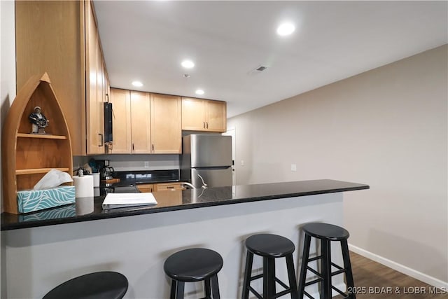 kitchen featuring stainless steel fridge, dark hardwood / wood-style floors, a kitchen bar, light brown cabinetry, and kitchen peninsula