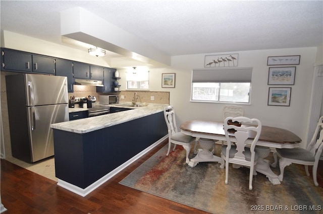 kitchen with under cabinet range hood, a peninsula, a sink, light countertops, and appliances with stainless steel finishes