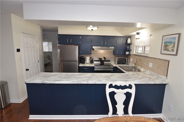 kitchen with sink, blue cabinetry, stainless steel appliances, decorative backsplash, and kitchen peninsula