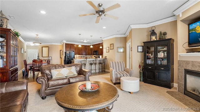 carpeted living room with ceiling fan, ornamental molding, and a tiled fireplace