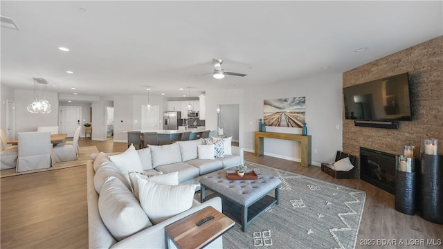 living room featuring hardwood / wood-style floors, ceiling fan with notable chandelier, and a fireplace