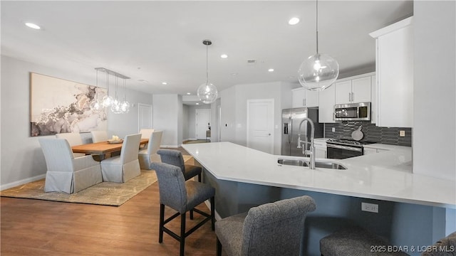 kitchen with a breakfast bar, kitchen peninsula, pendant lighting, stainless steel appliances, and white cabinets