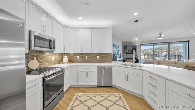 kitchen with sink, light hardwood / wood-style flooring, appliances with stainless steel finishes, hanging light fixtures, and white cabinets